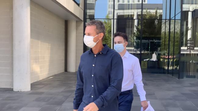 A support person (blue shirt) attempts to shield Christopher Middleton (white shirt) from cameras as he leaves the ACT Law Courts. Picture: Julia Kanapathippillai