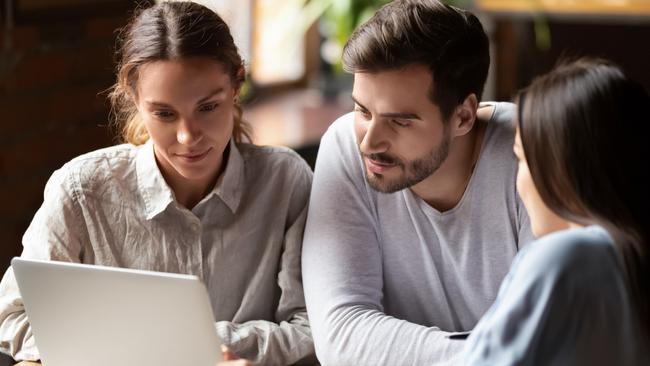 Realtor or insurance broker consulting young couple in cafe, sitting together at table, using laptop, looking at screen, financial advisor discussing mortgage or loan conditions with clients