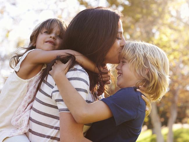 Mother Carrying Son And Daughter As They Play In Park