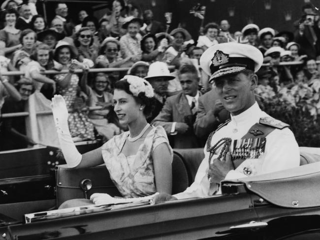 Queen Elizabeth II and Prince Philip wave from an open carriage as they drive past crowds of spectators at the Exhibition Grounds in Brisbane to watch a display of native dances in March 1954. Picture: Paul Popper/Popperfoto/Getty Images