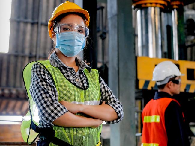 TRADESWOMAN/ TRADE WOMAN/ TRADESMAN/ TRADIE/BUILDING INDUSTRY: Factory woman worker or technician with hygienic mask stand with confident action with her co-worker  as background.