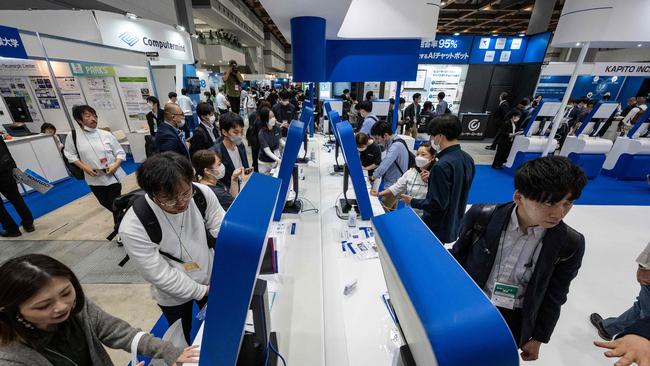 Visitors look at screens displaying Japanese company Tomorrow Net's navigation-type AI communication tool CAT.AI with a ChatGPT function.