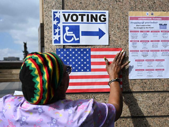 A poll worker hangs signs and a US flag outside a polling station during early voting ahead of the US midterm elections in Los Angeles, California, on November 1, 2022. (Photo by Robyn Beck / AFP)