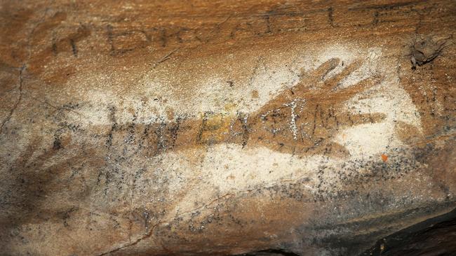 Graffiti scribbled over the top of indigenous art. Wonnarua elder Uncle Warren Taggart at one of at least five Hunter Valley caves where thieves have chiselled out indigenous art dating back thousands of years. Picture by Peter Lorimer.