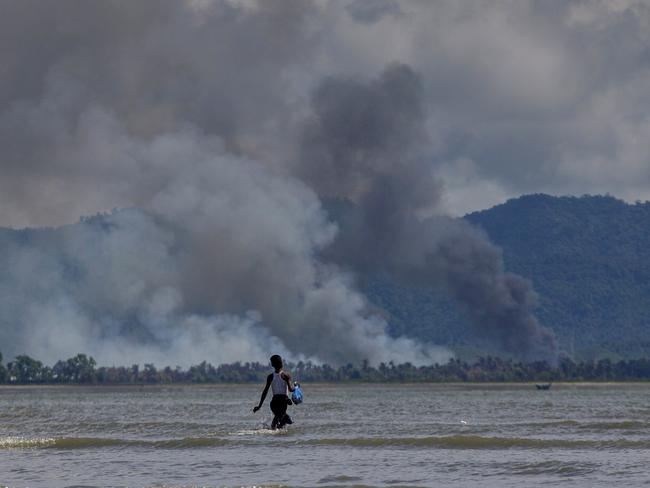 A Bangladeshi boy walks towards a parked boat as smoke rises from across the border in Myanmar. Picture: Dar Yasin/AP