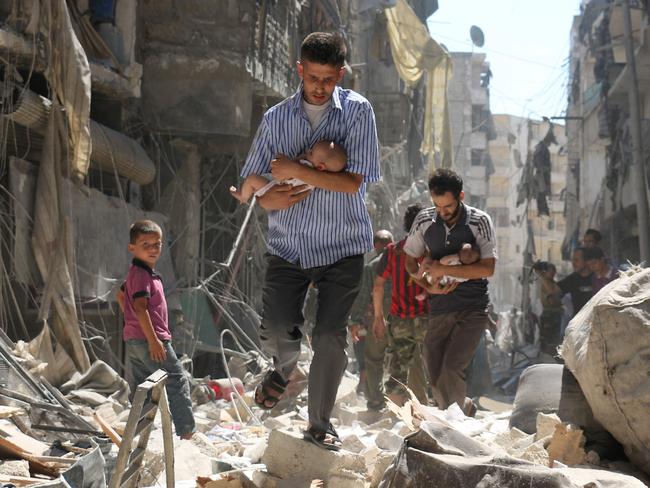 Syrian men carrying babies make their way through the rubble of destroyed buildings following a reported air strike on the rebel-held Salihin neighbourhood of the northern city of Aleppo, on September 11, 2016. Picture: AFP PHOTO / AMEER ALHALBI