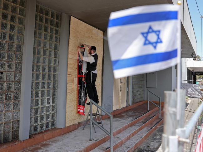 A member of the Jewish community staples a poster to the front of the damaged Adass Israel Synagogue. Picture: AAP