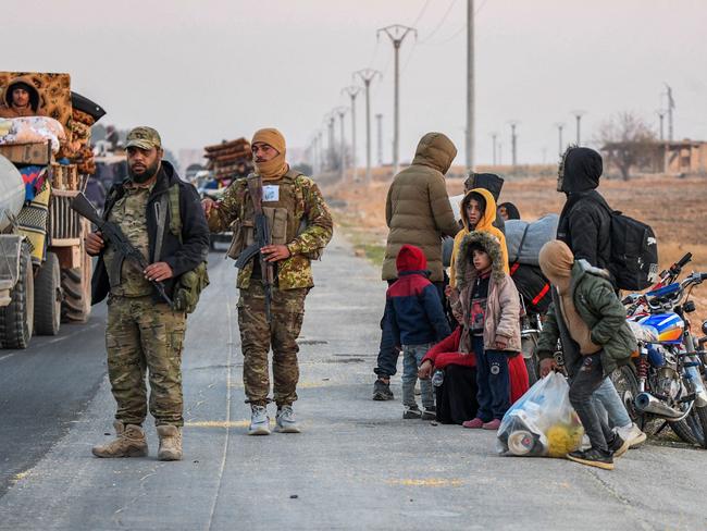 Anti-regime fighters stand on the roadside as displaced Syrian Kurds drive vehicles loaded with belongings on the Aleppo-Raqqa highway. Picture: AFP