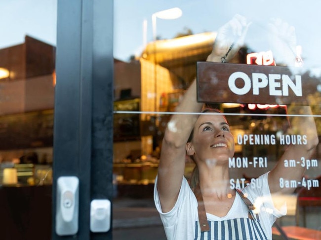 Portrait of a happy business owner hanging an open sign on the door at a cafe and smiling - food and drinks concepts