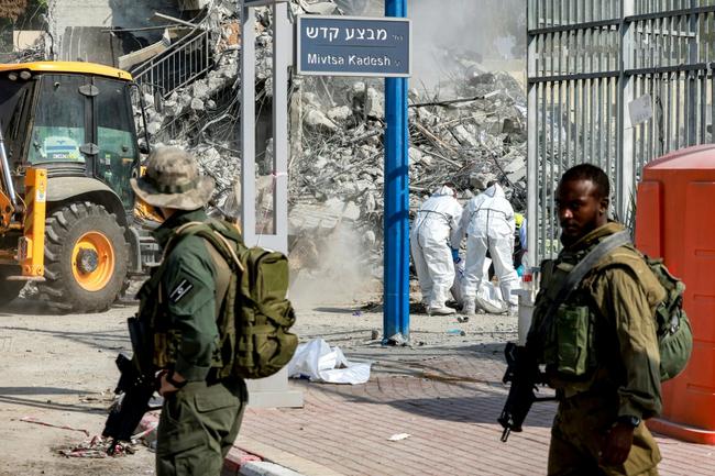 Israeli soldiers patrol as volunteers remove the bodies of killed Palestinian Hamas militants from outside the police station in Sderot on October 11, 2023