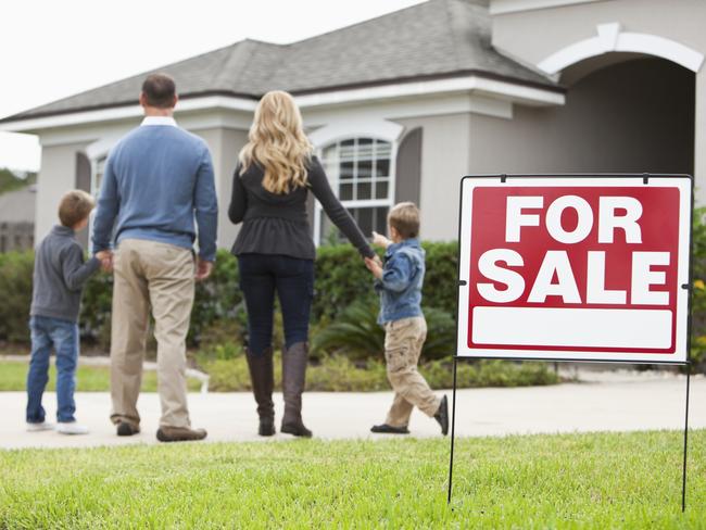 Family with two boys (4 and 6 years) standing in front of house with FOR SALE sign in front yard.  Focus on sign.