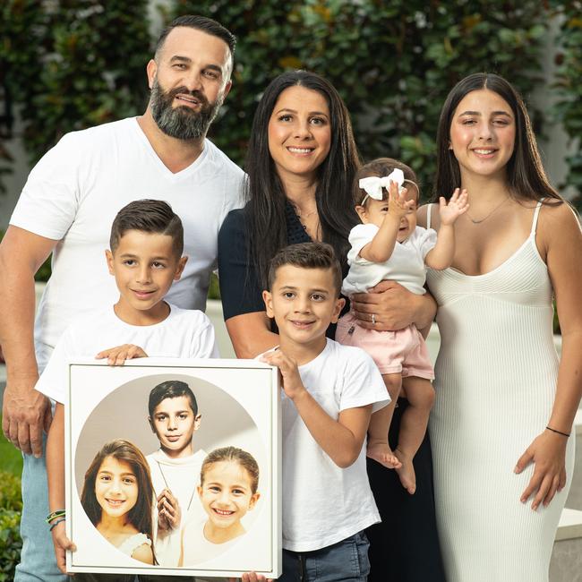 Danny and Leila Abdallah with Lan, 13, Alex, 8, Michael, 6, and Selina, 10 months, holding a picture of Anthony, 13, Angelina, 12, and Sienna, 8. Picture: Julian Andrews