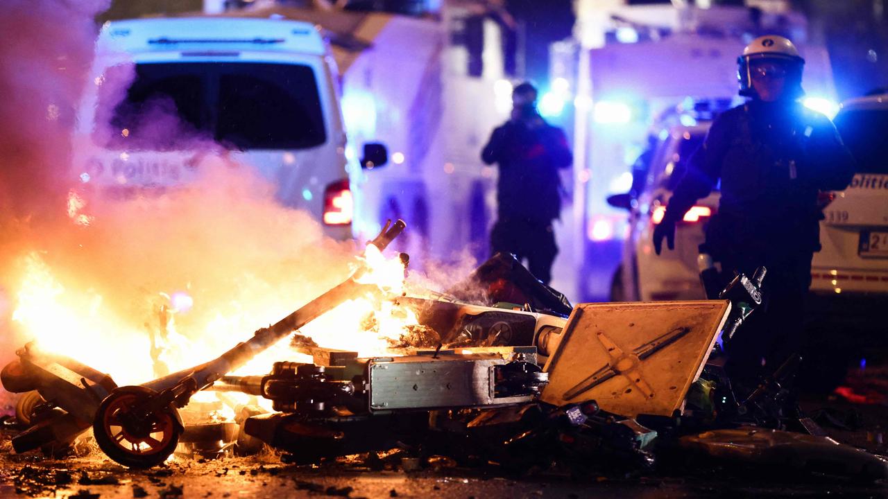 A police officer walks past burning electrical scooters on the sideline of the live broadcast of the Qatar 2022 World Cup Group F football match between Belgium and Morocco, in Brussels, on November 27, 2022. – Violence broke out in Brussels on November 27, 2022 after Morocco's victory over Belgium at the World Cup, with "dozens of people" attacking street furniture and police, police said. (Photo by Kenzo TRIBOUILLARD / AFP)