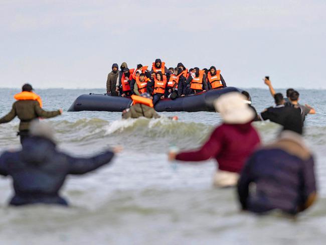 TOPSHOT - Migrants wave to a smuggler's boat in an attempt to cross the English Channel, on the beach of Gravelines, near Dunkirk, northern France on April 26, 2024. Five migrants, including a seven-year-old girl, died on April 23, 2024 trying to cross the Channel from France to Britain, local authorities said, just hours after Britain passed a controversial bill to deport asylum seekers to Rwanda. (Photo by Sameer Al-DOUMY / AFP)