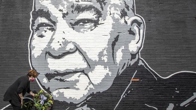A fan places a wreath below a mural of singer John Prine, painted by Graham Allen of SquarePegs Studio and Design, in Lexington, Kentucky, following the death of the singer-songwriter on April 7. Picture: Ryan C. Hermens/Lexington Herald-Leader via AP.