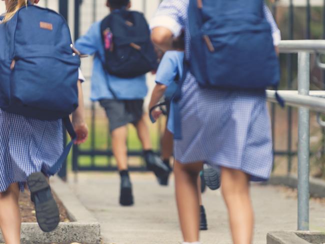 School children running away. They are wearing uniforms and carrying backpacks. They are having a race. Multi ethnic group with Asian, Caucasian and Aboriginal children. Rear view