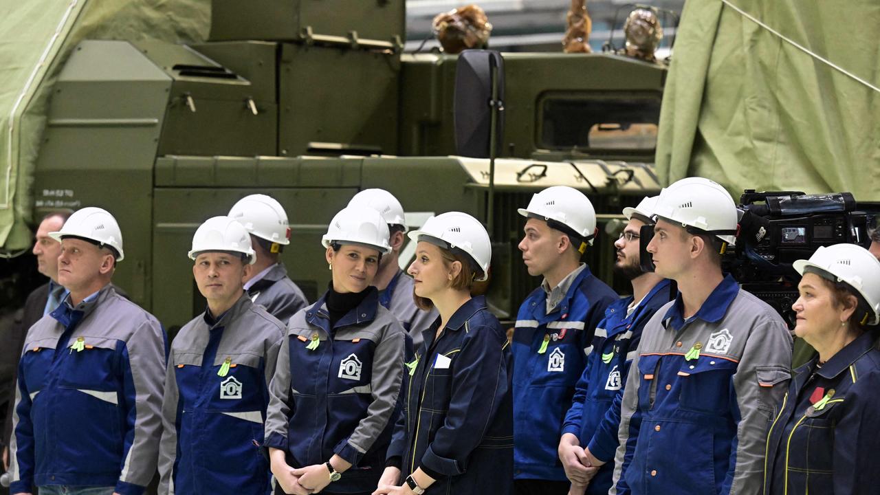 Workers stand in front of military vehicles at the plant as Putin speaks (Photo by Ilya Pitalev / SPUTNIK / AFP)