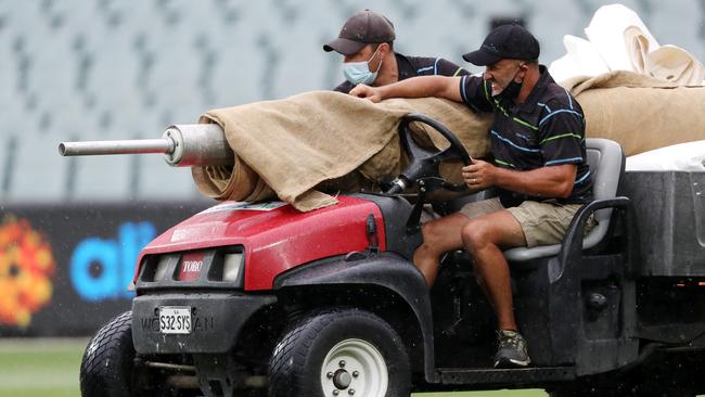 Head curator, Damian Hough and his ground staff start to cover the pitch as the rain comes down in Adelaide.