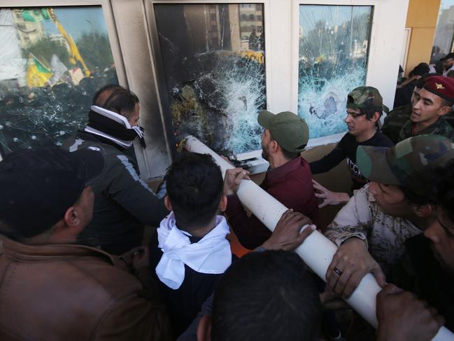 Iraqi protesters use a plumbing pipe to break the bullet-proof glass of the US embassy's windows in Baghdad. Picture: AFP