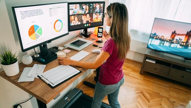 Woman working from home at standing desk is walking on under desk treadmill