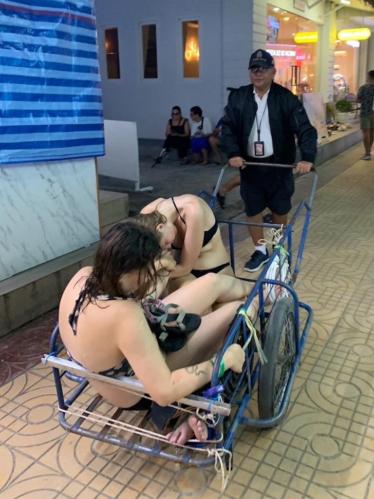 This is the wholesome moment a caring policeman used a trolley to wheel two drunk and unconscious female backpackers to their hotel Picture: Viralpress.