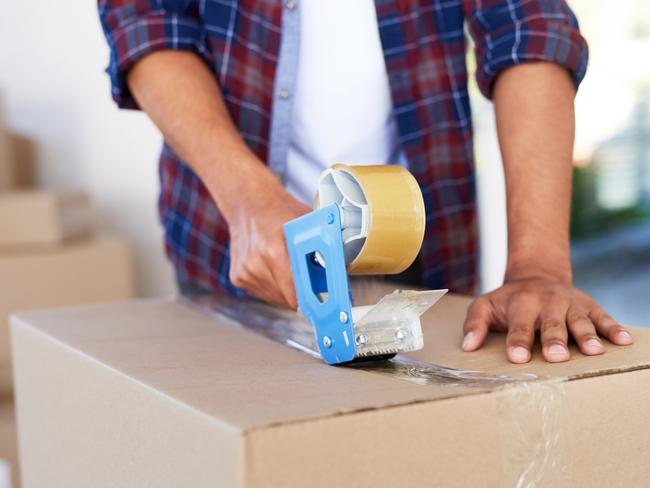 Shot of an unidentifiable man using a tape dispenser to close a box while moving house