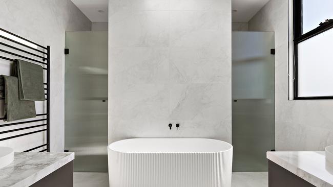 This hotel-inspired bathroom features a rainfall shower, marble benchtops, and sleek black tapware.