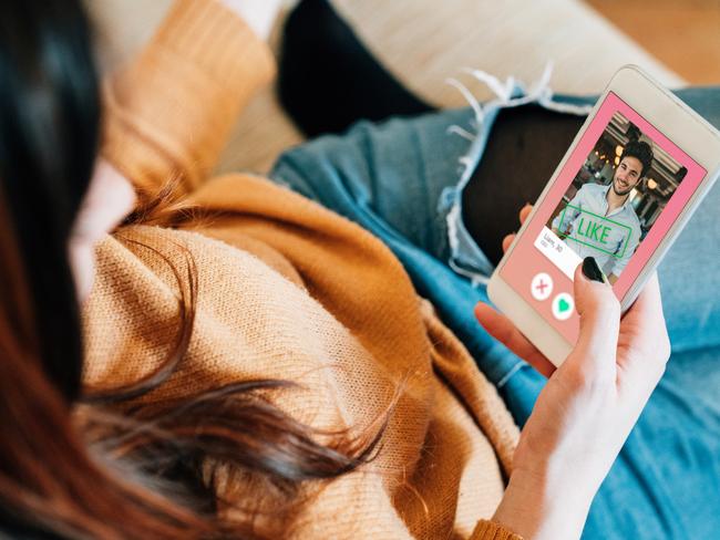 Young adult woman swiping on an online dating app. She's using her smart phone on the sofa at home.