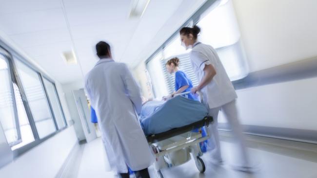 A motion blurred photograph of a patient on stretcher or gurney being pushed at speed through a hospital corridor by doctors & nurses to an emergency room