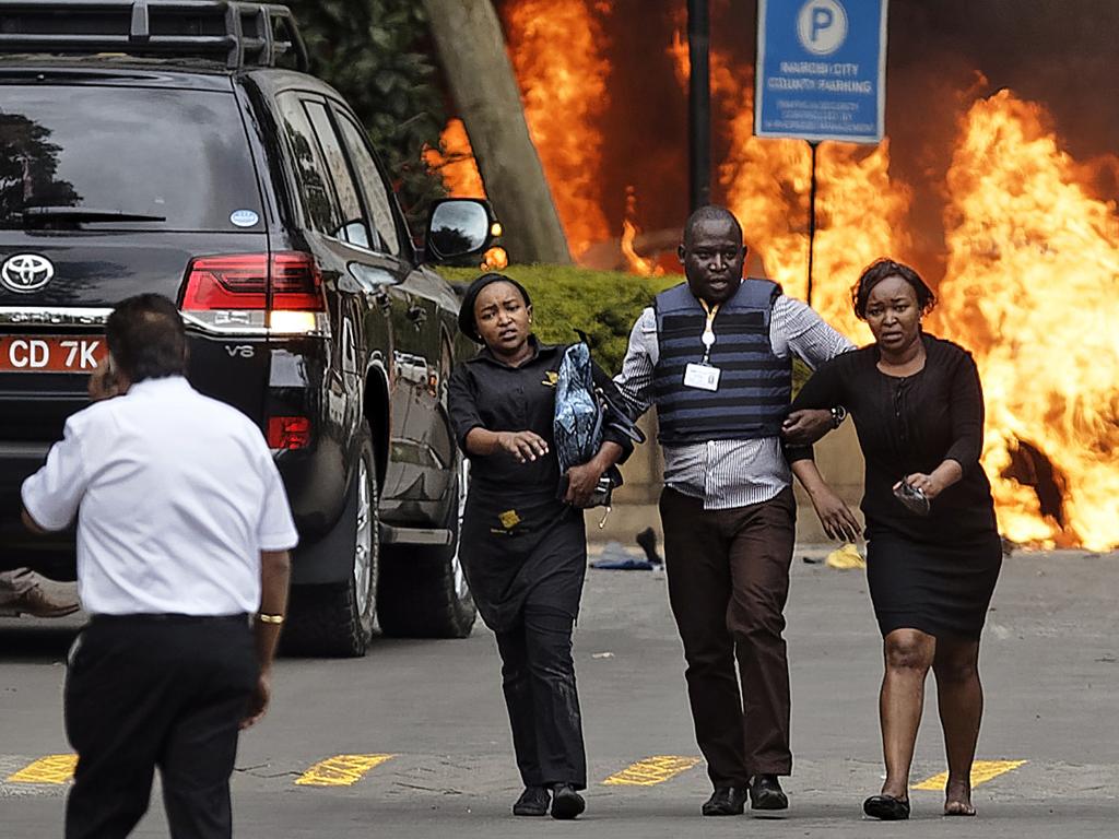 Security forces help civilians flee the scene as cars burn behind, at a hotel complex in Nairobi. Picture: AP