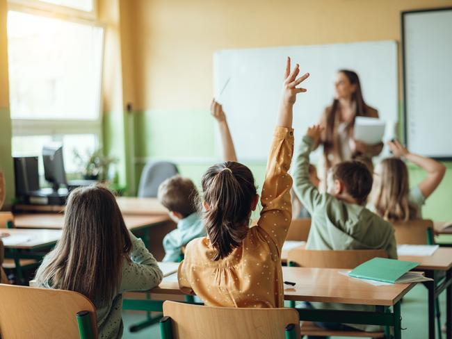 Students raising hands while teacher asking them questions in classroom