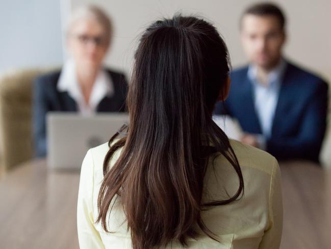 Businesswoman and businessman HR manager interviewing woman. Candidate female sitting her back to camera, focus on her, close up rear view, interviewers on background. Human resources, hiring concept