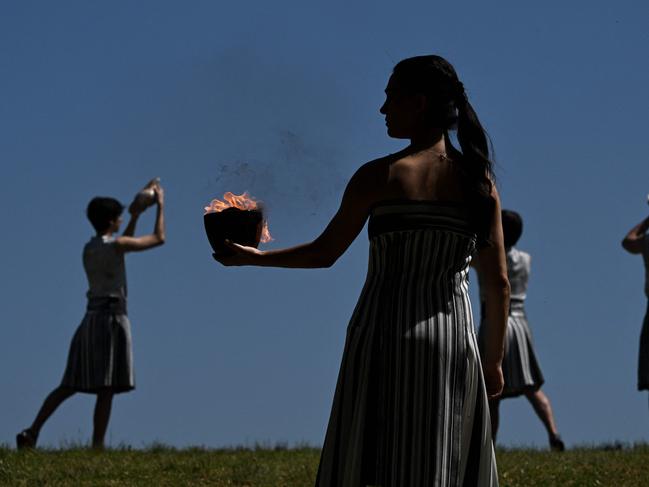 A woman in the role of a priestess holds the Olympic flame after lighting it during the rehearsal of the flame lighting ceremony for the Paris 2024 Olympics Games at the ancient temple of Hera on the Olympia archeological site, birthplace of the ancient Olympics in southern Greece, on April 15, 2024. (Photo by Aris MESSINIS / AFP)