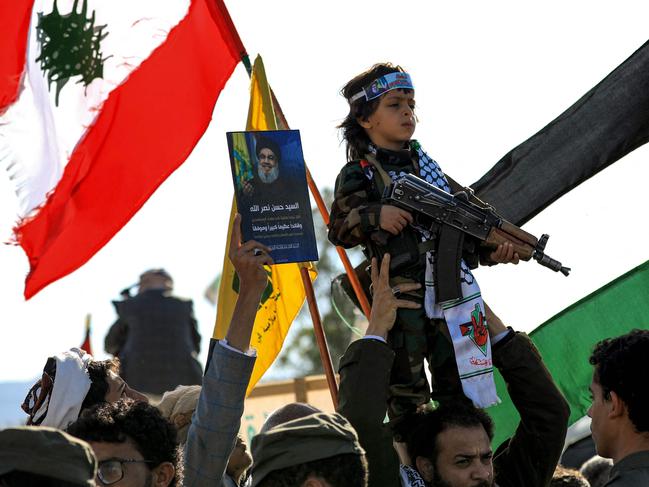 A man carries on his shoulders a young child holding an assault rifle and wearing military fatigues during a rally held in the Huthi-controlled capital Sanaa on October 18, 2024 in protest against Israel's attacks on Lebanon and the ongoing war between Israel and Hamas militants in the Gaza Strip. Israel announced on October 17 the killing of Hamas' leader Yahya Sinwar, mastermind of the October 7 attack, calling his death a "heavy blow" to the Palestinian group it has been fighting for more than a year. (Photo by Mohammed HUWAIS / AFP)