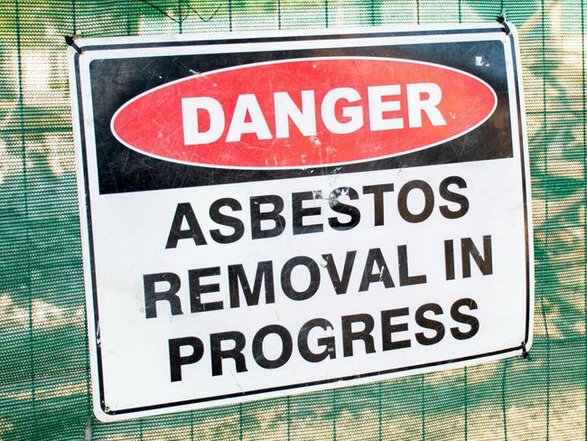 A warning sign Danger Asbestos on a fence at construction site where old house is demolishing  - picture istock