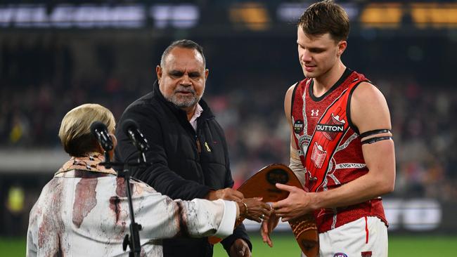 Essendon star Jordan Ridley accepts the Yiooken Trophy from Michael Long (centre) and Aunty Pam Pedersen as best on ground in the Dreamtime at the ‘G clash. Picture: Morgan Hancock / Getty Images