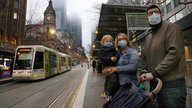 A family wait in face masks wait for a tram in Collins street, Melbourne, on Thursday. Picture: David Crosling