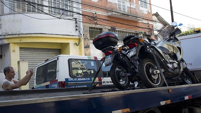 A bystander in the Rio de Janeiro favela of Morro dos Prazeres takes photos as two motorcycles that belonged to Italian tourists are taken away by authorities after one of the men was shot dead. Picture: AP/Silvia Izquierdo