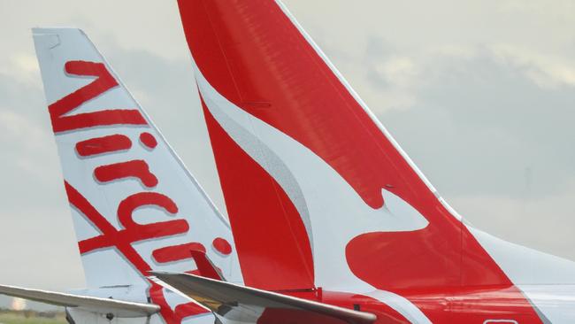 The vertical stabilisers of a Qantas Boeing B737-838 plane, registration VH-VZQ, and a Virgin Australia Boeing B737-8FE plane, registration VH-VUZ, waiting at the northern end of the main runway of Sydney Kingsford-Smith Airport in preparation for departure.  The Qantas plane is heading to Adelaide as flight QF741 and the Virgin plane is heading to Adelaide as flight VA428.  In the background is another Virgin B737-8FE plane. This image was taken from Nigel Love Bridge, Mascot on a sunny afternoon on 3 December 2023.