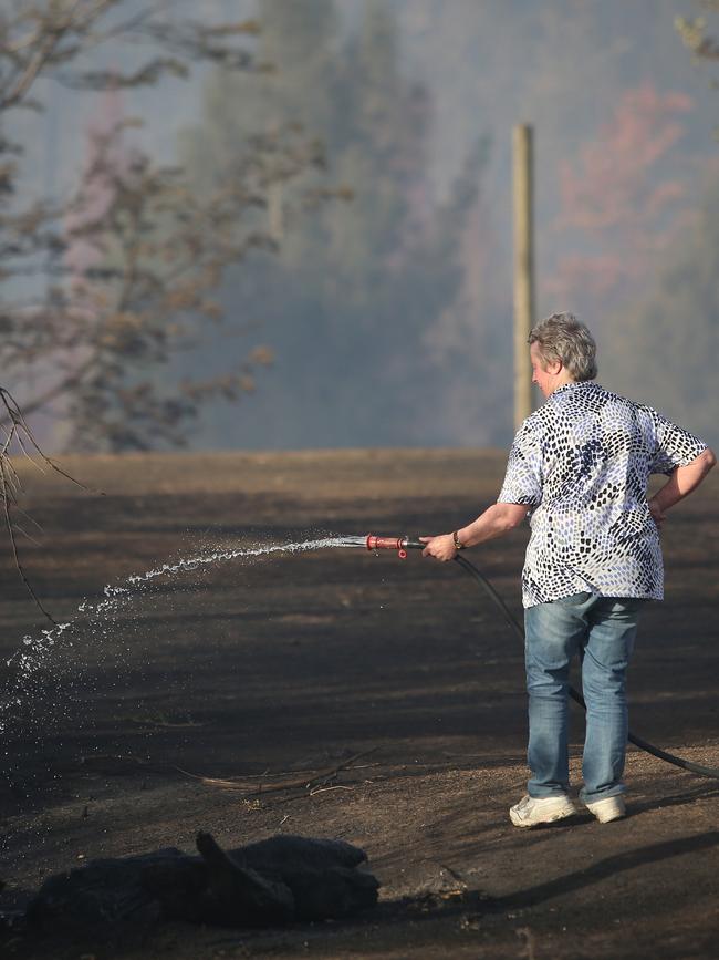 Alice Britten helps keep her property moist after firefighters saved her house. Picture: Peter Lorimer