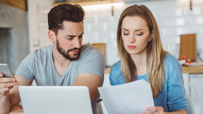 Young couple worried about their finances at home. They are wearing pajamas and drinking first coffee of the day at the kitchen.