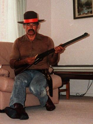 Ivan Milat, wearing a sheriff's badge, poses in his lounge room with firearms.