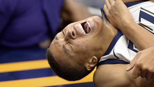 Dante Exum grimaces as he grabs his left shoulder after hitting the deck under the net.