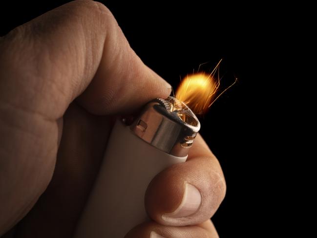 Hand lightning a lighter with a flame freezed in motion on a black background.