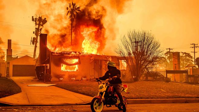 A motorcyclist stops to look at a burning home in the Altadena area of LA. PIcture: AFP