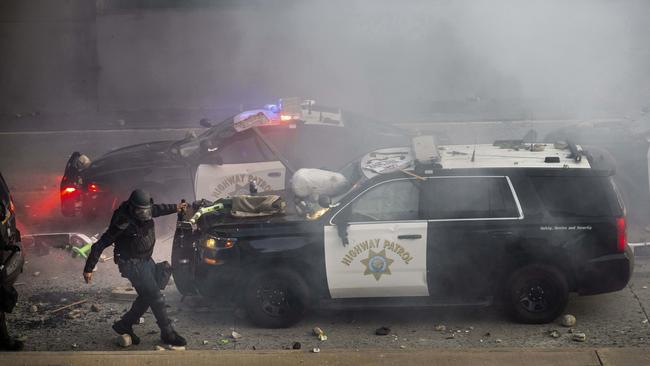 A California Highway Patrol officer pulls an electric scooter off a vehicle on a highway as protesters throw objects at the police vehicles in downtown Los Angeles. Picture: AP Photo/Ethan Swope