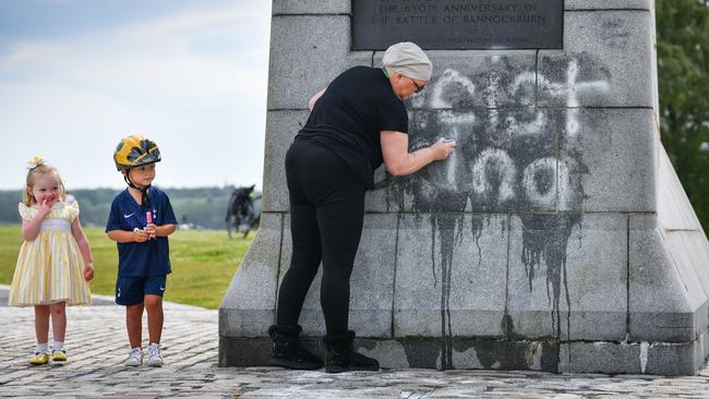 Children look on as a member of the public cleans the Robert the Bruce Statue which has been defaced with graffiti saying "Racist King" on June 12 following a Black Lives Matter protest. Picture: Getty