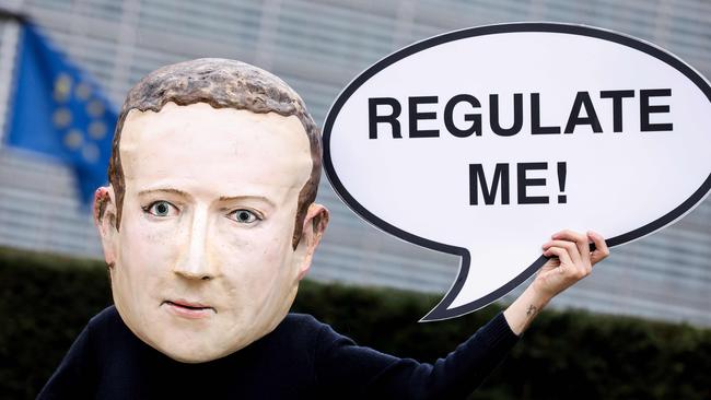 An activist wearing a mask depicting Facebook CEO Mark Zuckerberg holds a banner reading "Regulate me" during an action marking the release of the Digital Services Act, outside the European Commission building in Brussels in 2020.