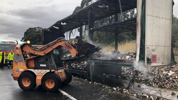 Crews work to remove debris from the road after the truck fire destroyed the trailer and all goods onboard.