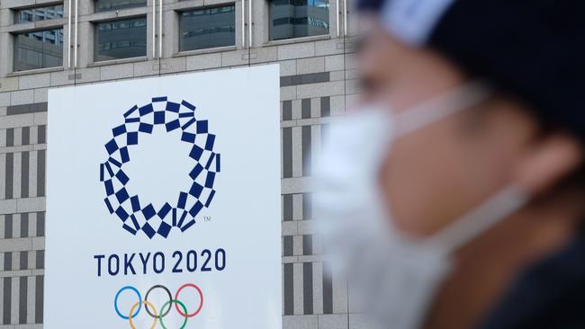 A man wearing a mask passes the logo of the Tokyo 2020 Olympic Games